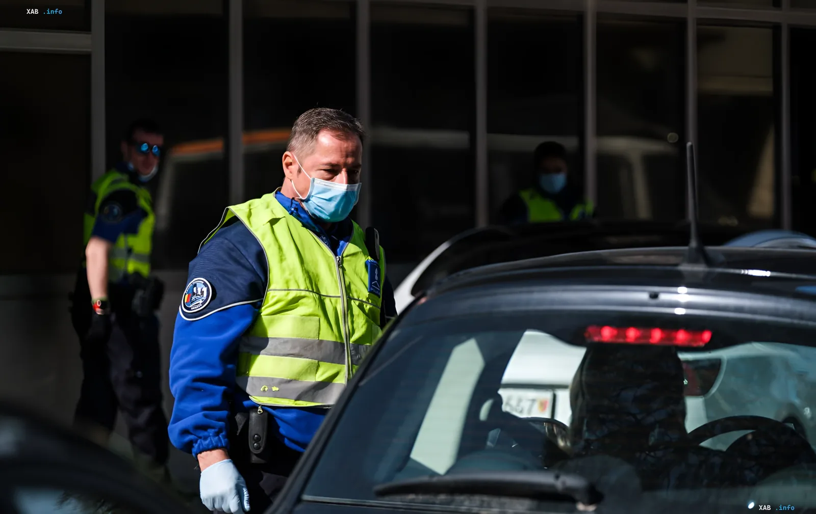 Französischer Polizist in Maske und Weste steht neben einem Auto vor einem Gebäude, was die EU-Grenzkontrolle und Sanktionen gegen russische Militärangehörige illustriert