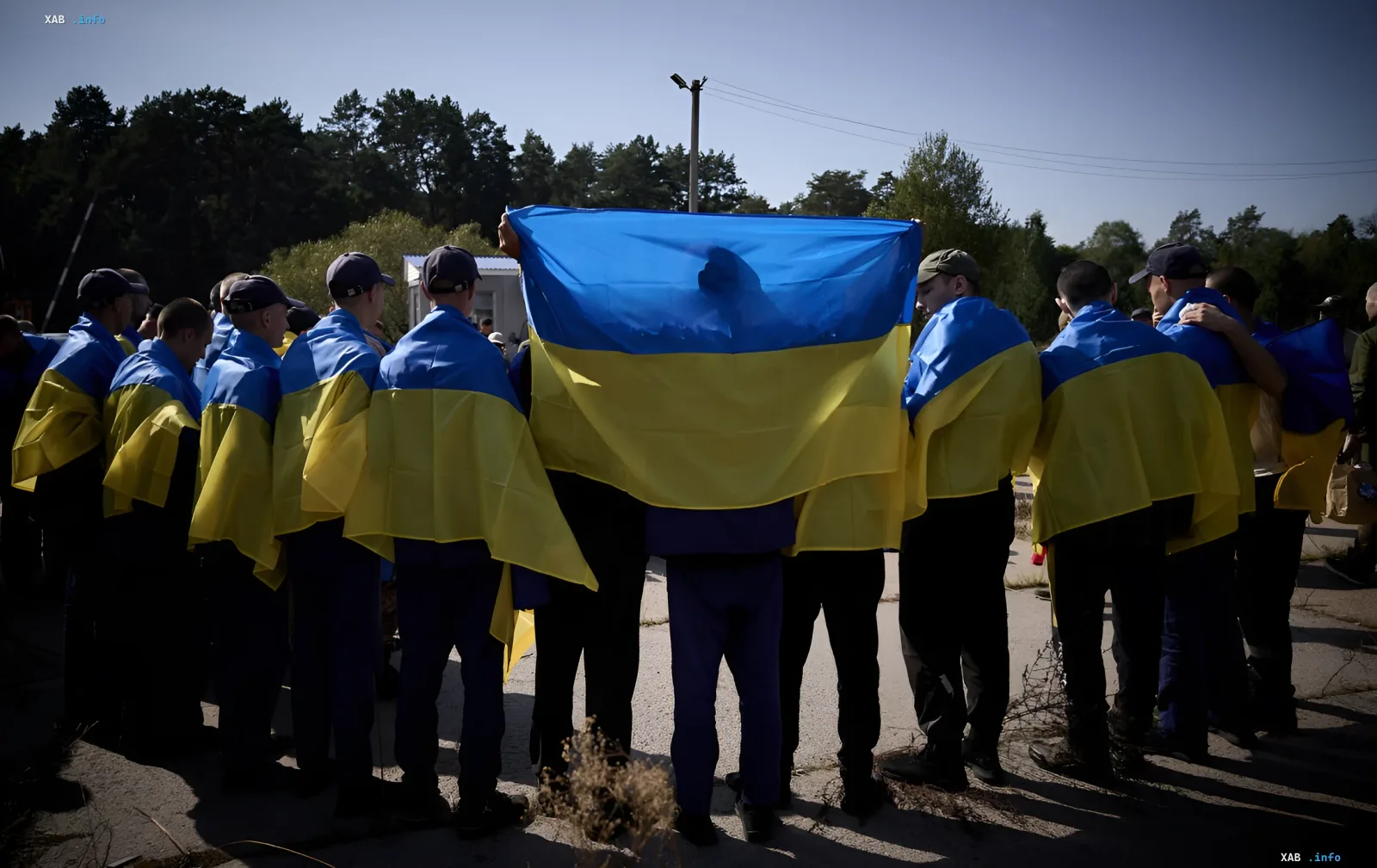 Gruppe von Menschen in ukrainischen Flaggen steht mit dem Rücken zur Kamera und hält eine große ukrainische Flagge — Symbol der Hoffnung auf Gefangenenaustausch