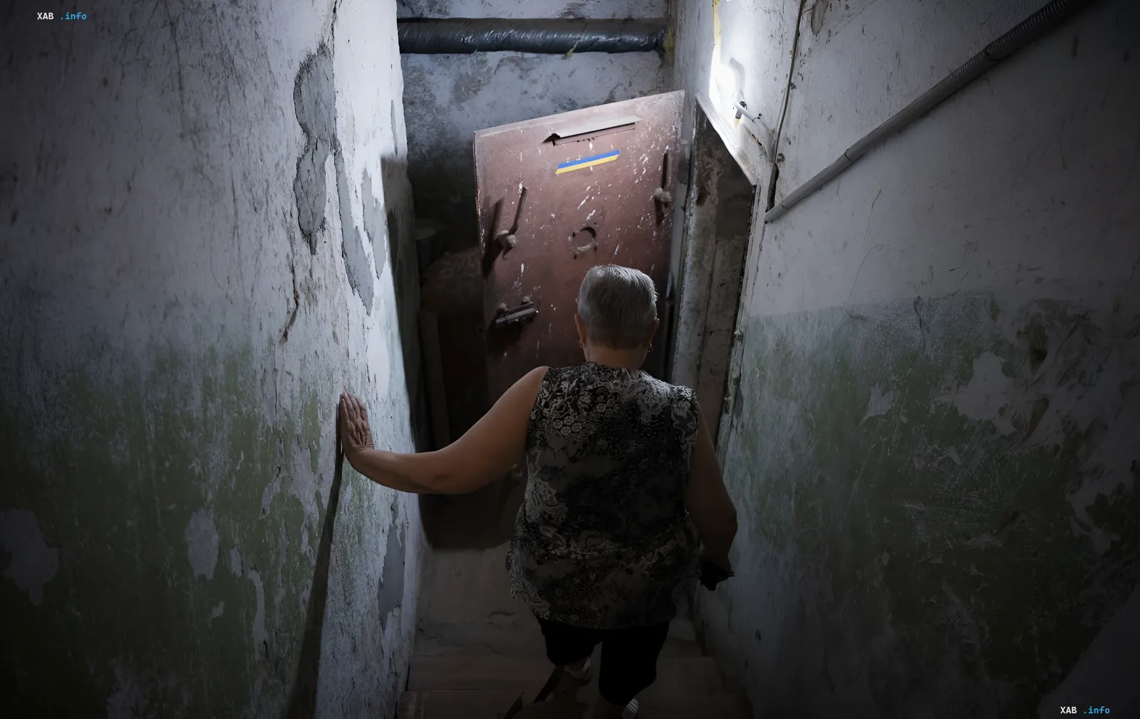 Woman descends into a basement through a heavy metal door with a Ukrainian flag in Chernihiv after a series of explosions on the night of June 28