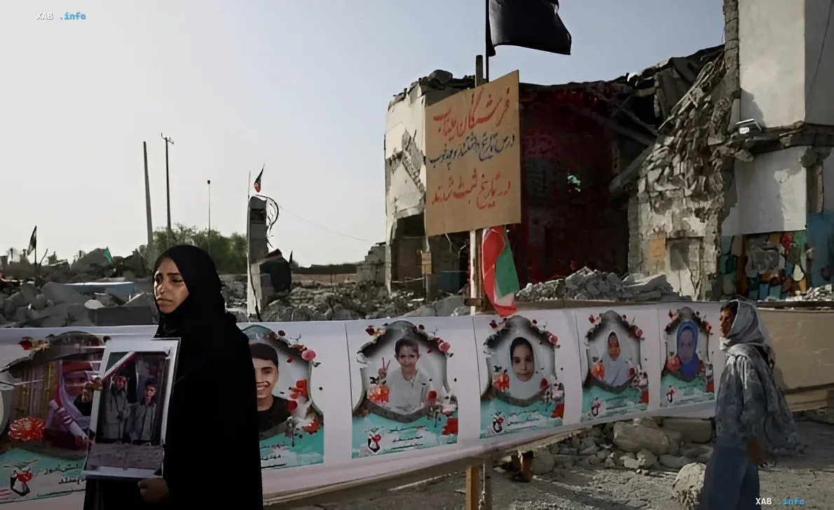 Frau im schwarzen Hijab steht an einem Denkmal mit Porträts verstorbener Kinder vor einem zerstörten Schulgebäude im Iran
