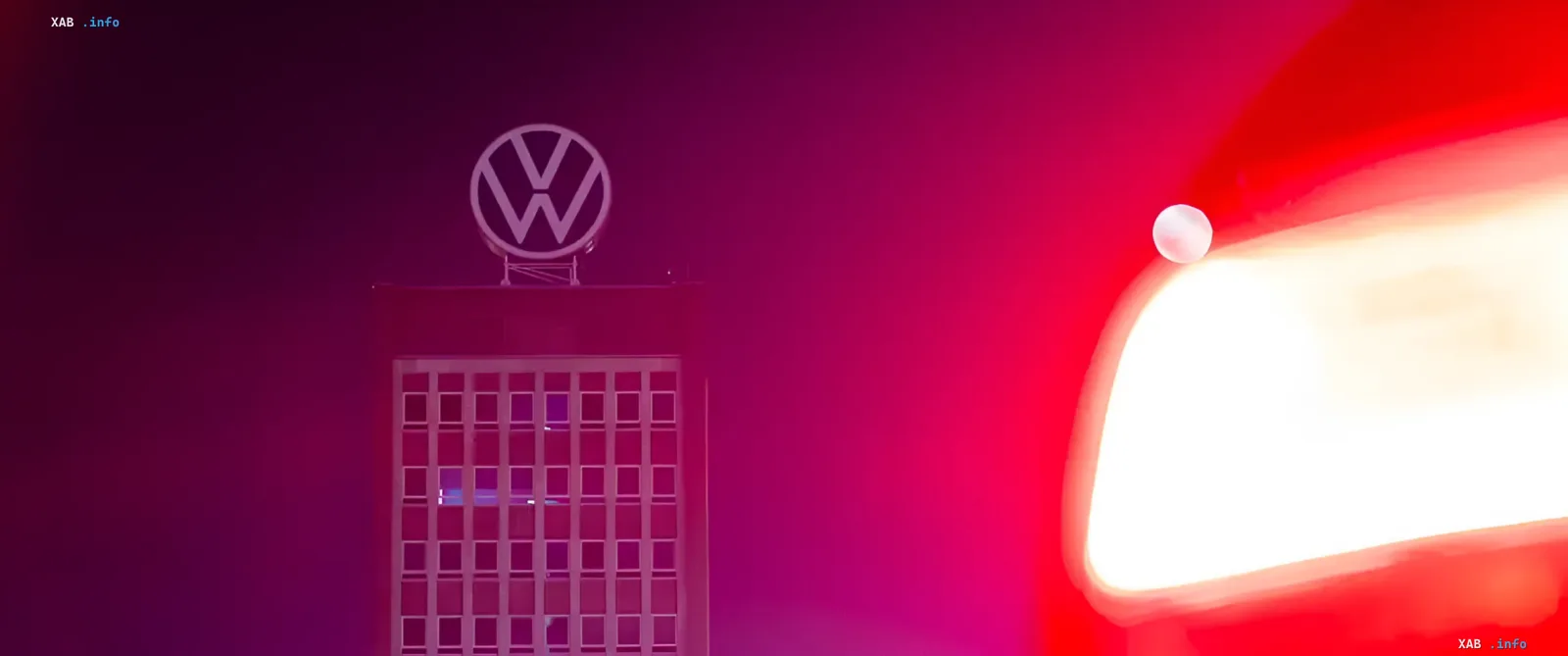 Логотип Volkswagen на здании завода в Германии на фоне красного света фар автомобиля, символизирующий кризис в автопроме