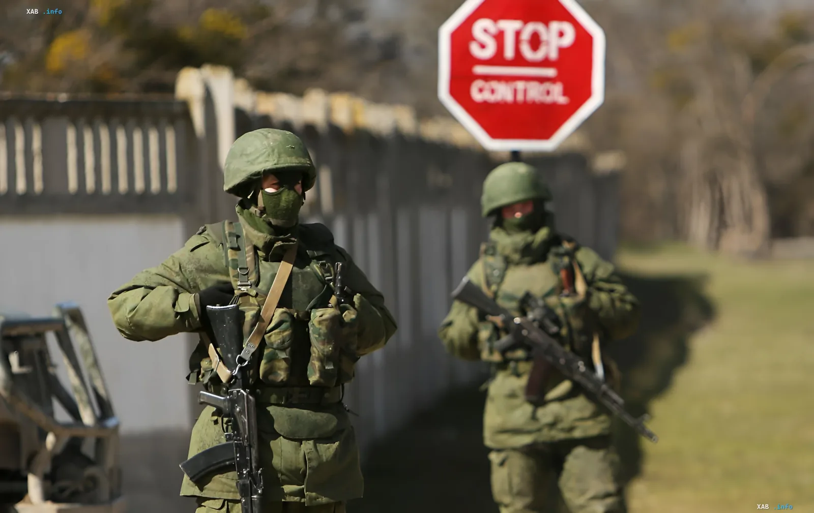 Soldaten in Tarnanzug und Masken mit Gewehren bei einem 'STOP CONTROL'-Schild, die das Thema 'kleine grüne Männchen' und Provokationen gegen die NATO veranschaulichen