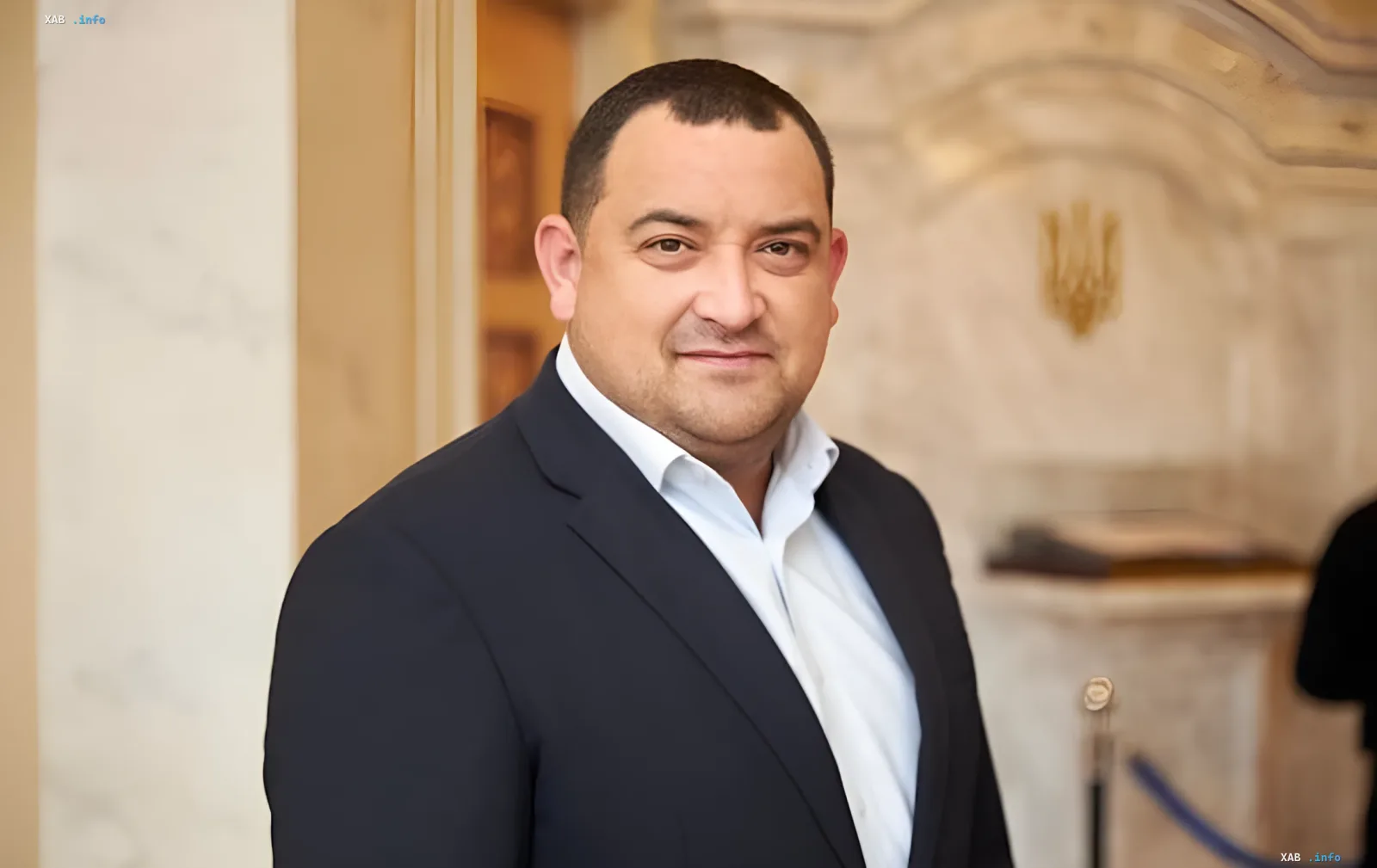 Abgeordneter der Partei 'Diener des Volkes' im Anzug vor ukrainischem Staatswappen — Beschuldigter in NABU-Korruptions- und Gerichtsumgehungsfall