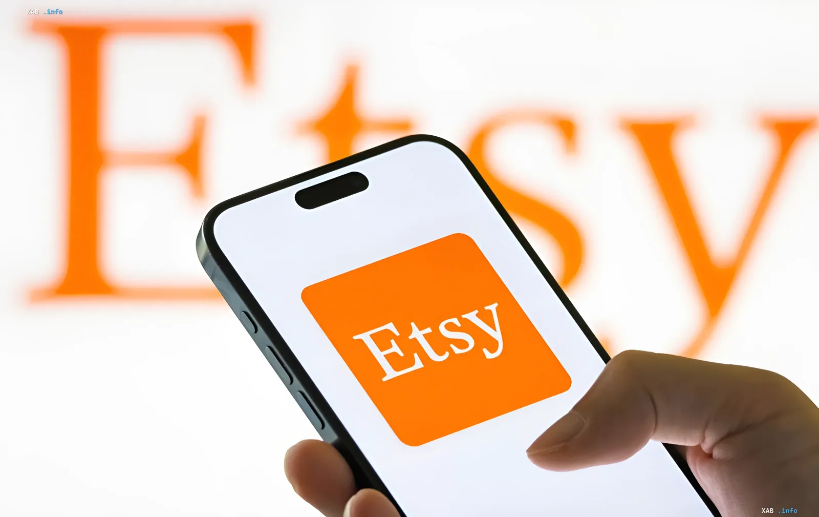 Smartphone mit Etsy-Logo in der Hand vor einem unscharfen orangefarbenen Etsy-Logo-Hintergrund – Illustration der Automatisierung des Exports ukrainischer Waren über die Plattform