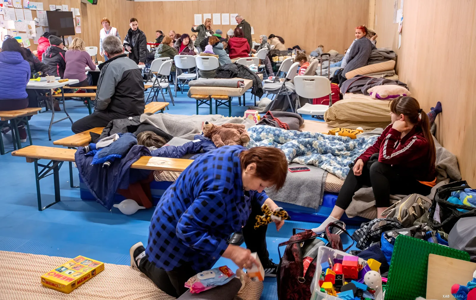 Ukrainian refugees in a temporary shelter: women and children resting on mattresses surrounded by belongings