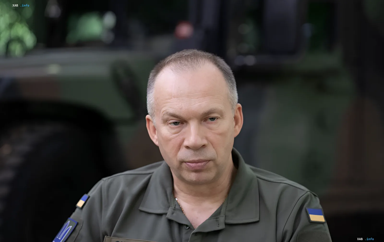 Witalij Syrsky in Militäruniform mit ukrainischen Flaggen an den Ärmeln, vor militärischer Ausrüstung, kommentiert die Situation mit dem Verteidigungsministerium