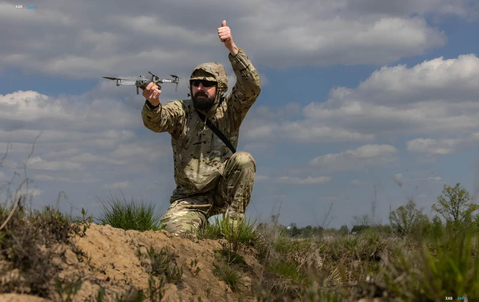 A Ukrainian soldier in camouflage holds a military drone and gives a thumbs-up, symbolizing reliable supply of unmanned aerial vehicles on the front line.