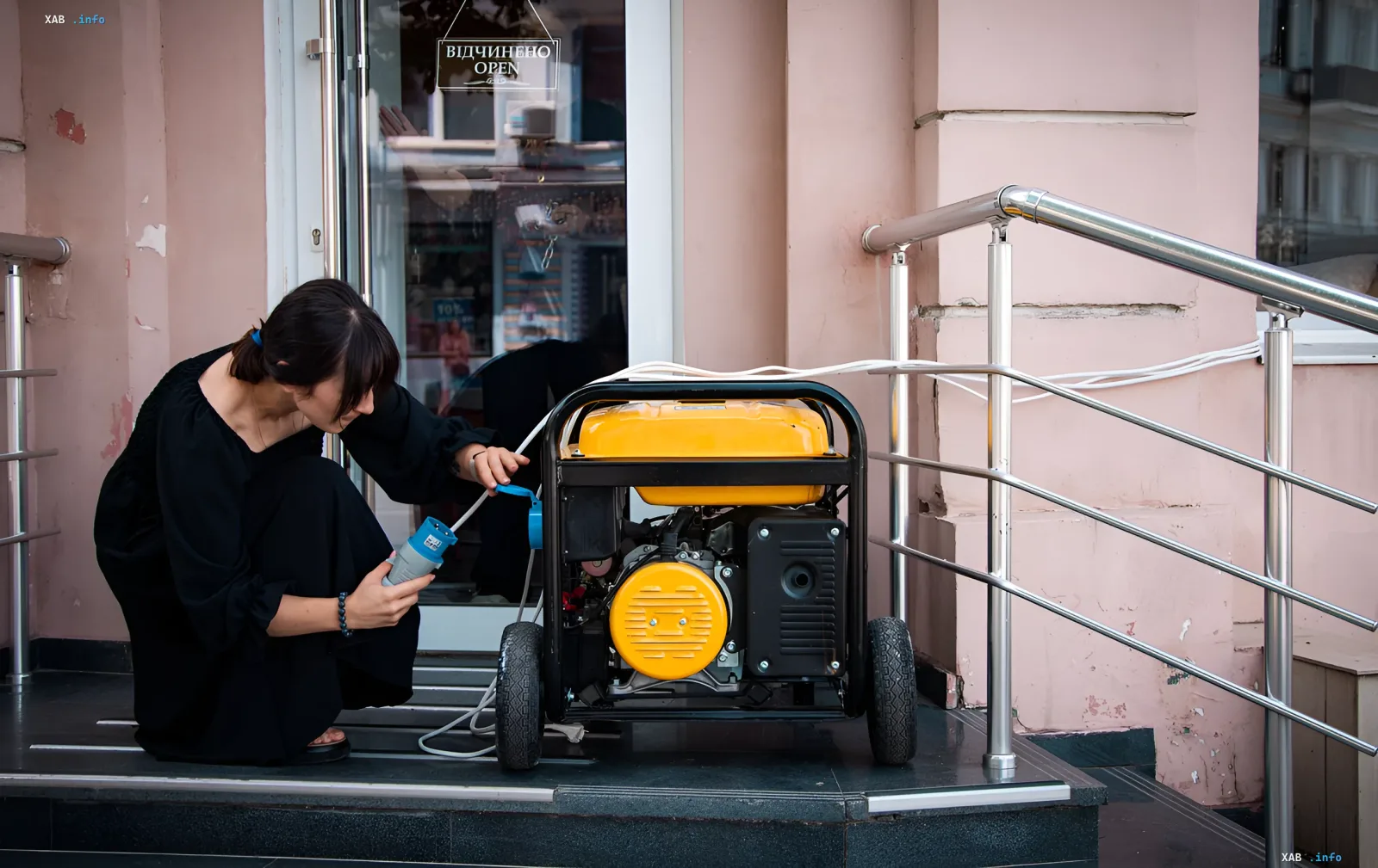 Woman connects a gasoline generator to a building in Ukraine due to power outages, while an 'Open' sign hangs on the door