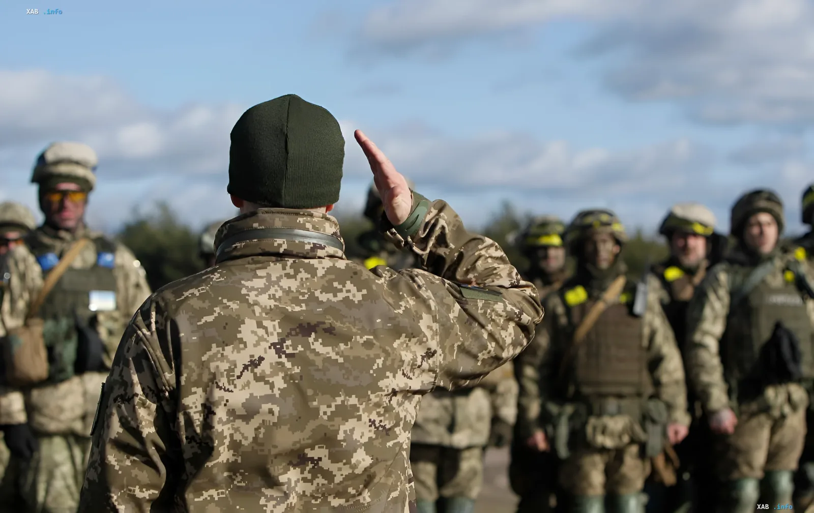Officer in camouflage gives orders to a group of mobilized soldiers against the sky