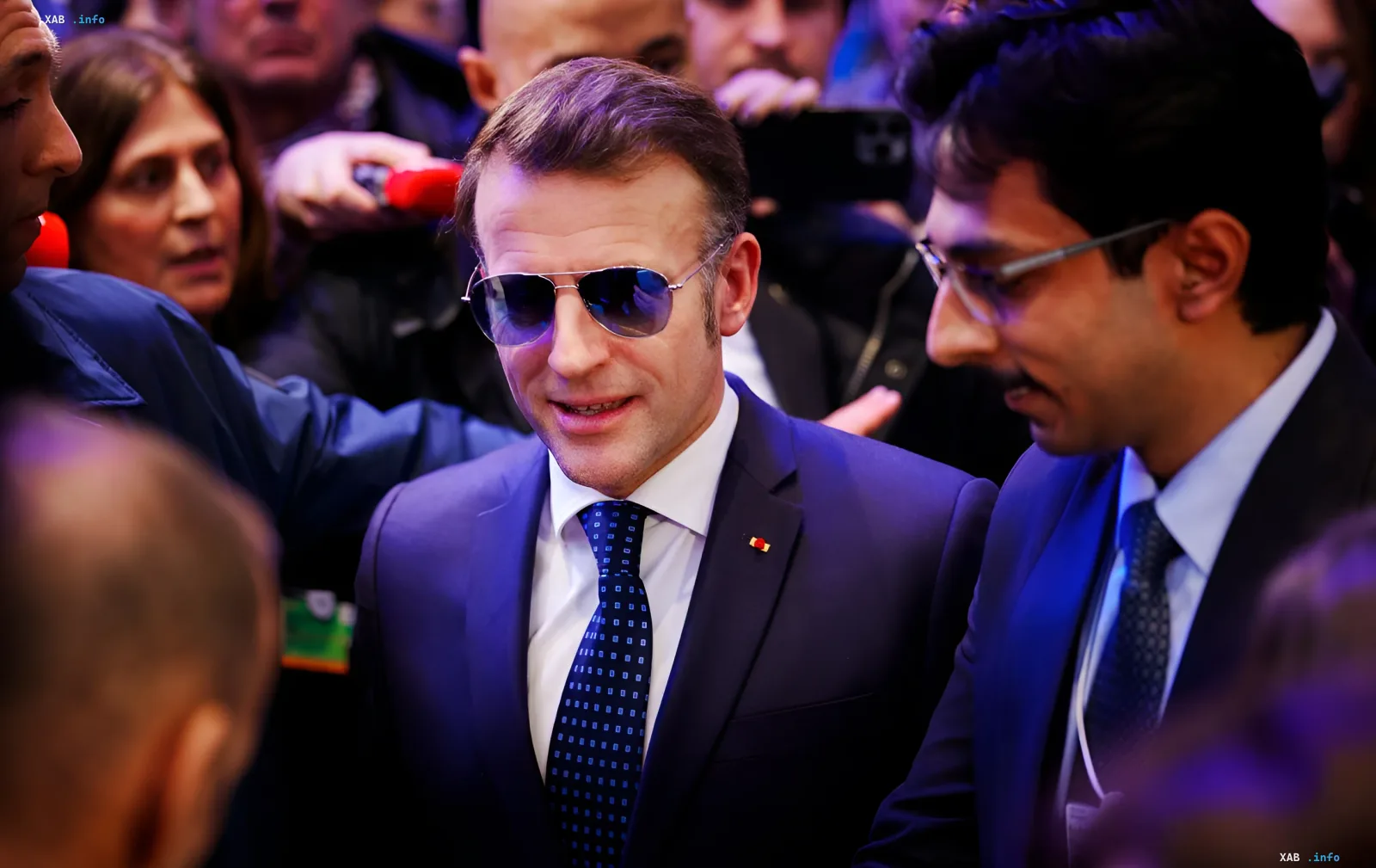 Emmanuel Macron in sunglasses and suit among journalists, discussing plans for the 2027 presidential elections