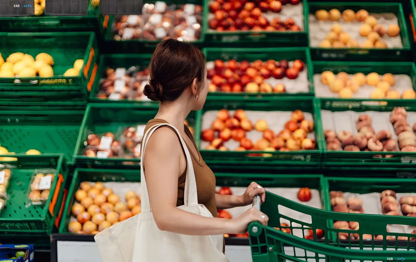 Frau mit einem Korb wählt Früchte in einem Supermarkt vor einem Hintergrund von grünen Kisten mit Produkten