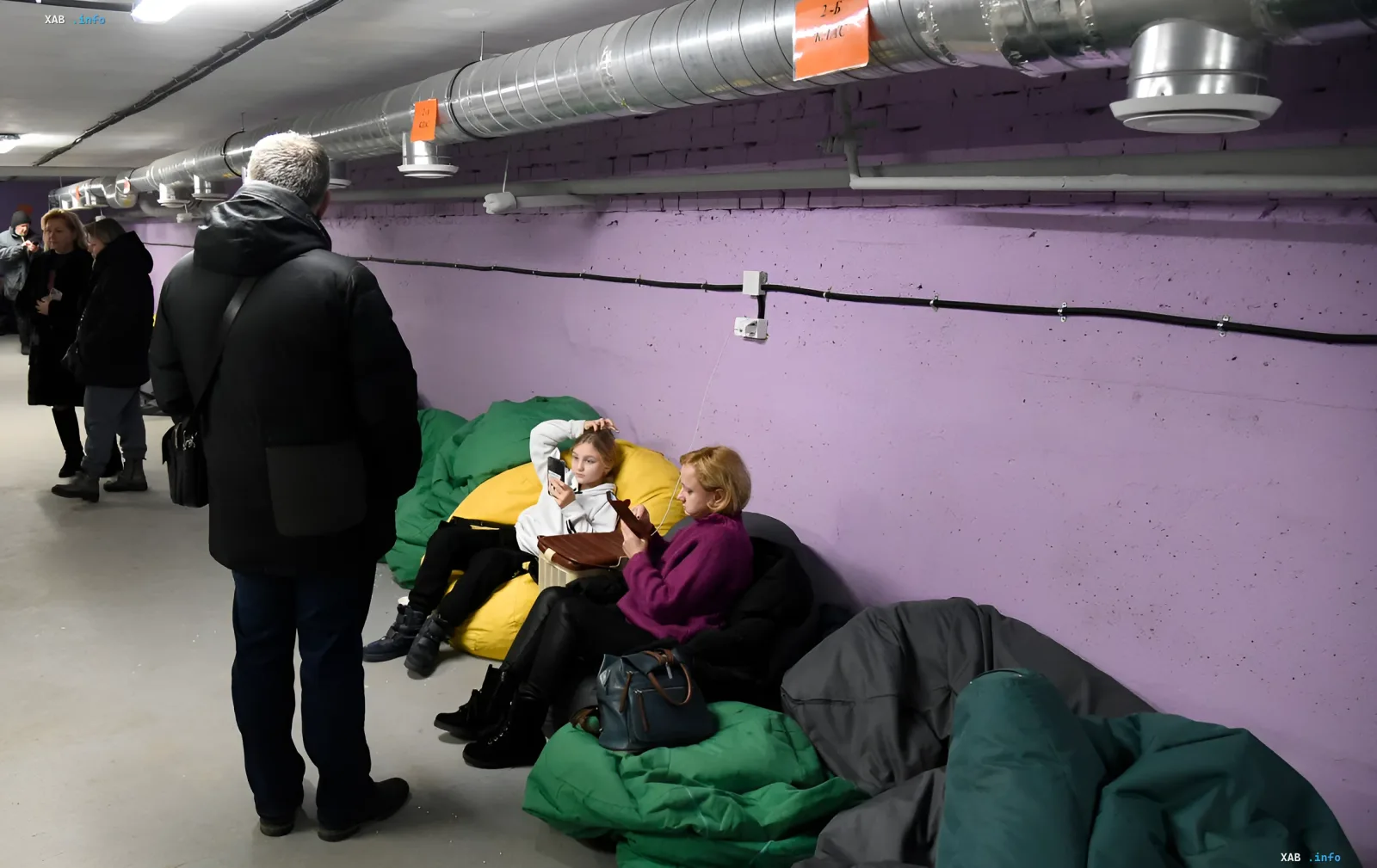 Женщины сидят на мешках в бомбоубежище и пытаются найти связь на смартфонах