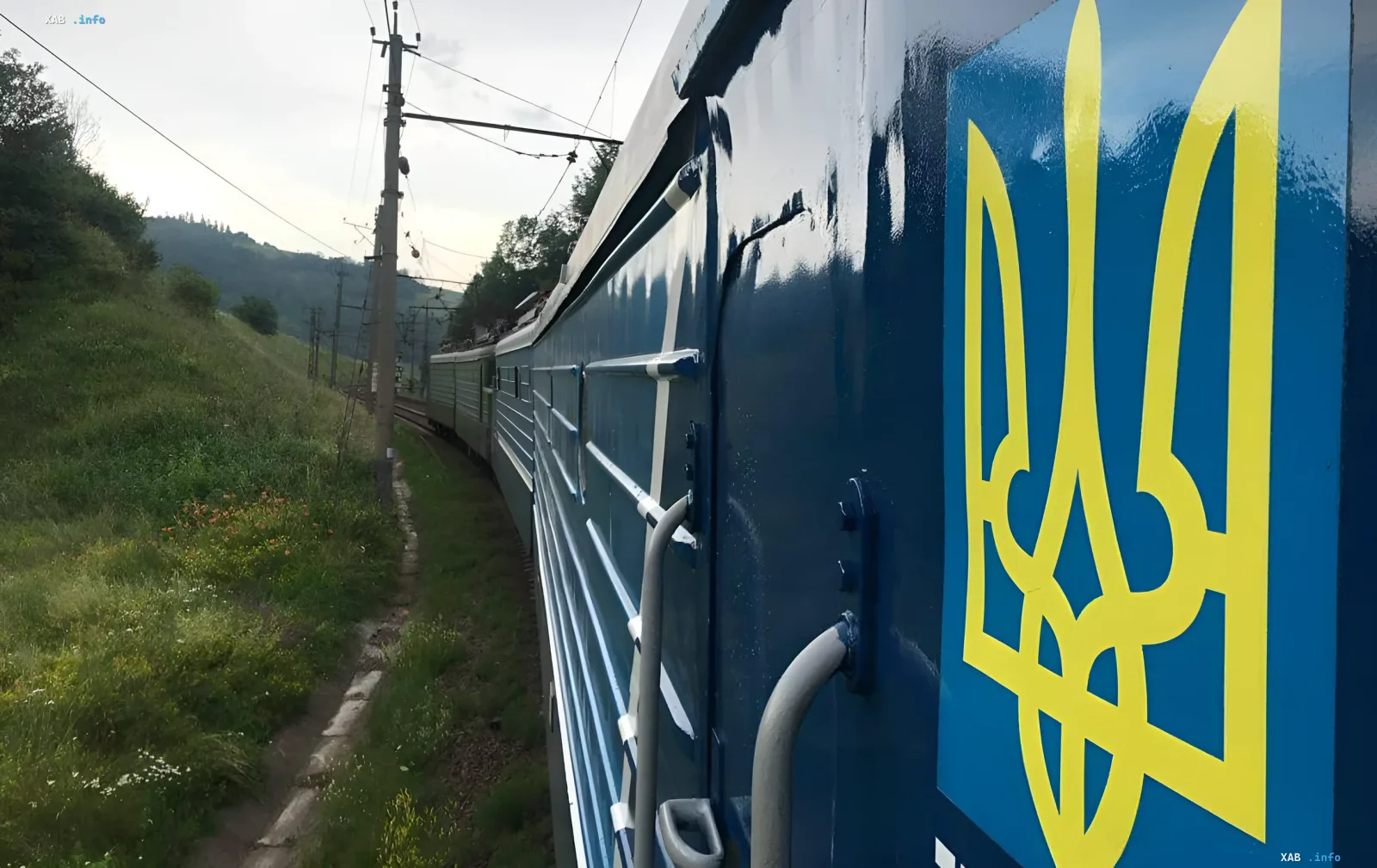 Ukrzaliznytsia train with yellow trident on blue background moving through countryside, illustrating mass delays due to border and route issues