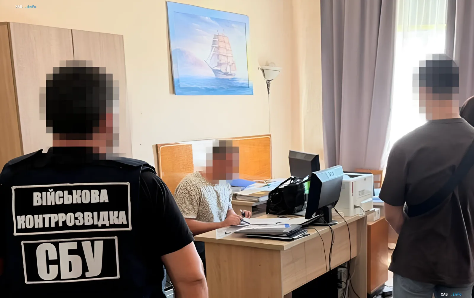 Співробітник СБУ в жилеті з написом 'Військова контррозвідка СБУ' проводить допит в кабінеті, де сидить затриманий доцент Міноборони України, звинувачений у шпигунстві на користь ГРУ та злитті креслень дронів.