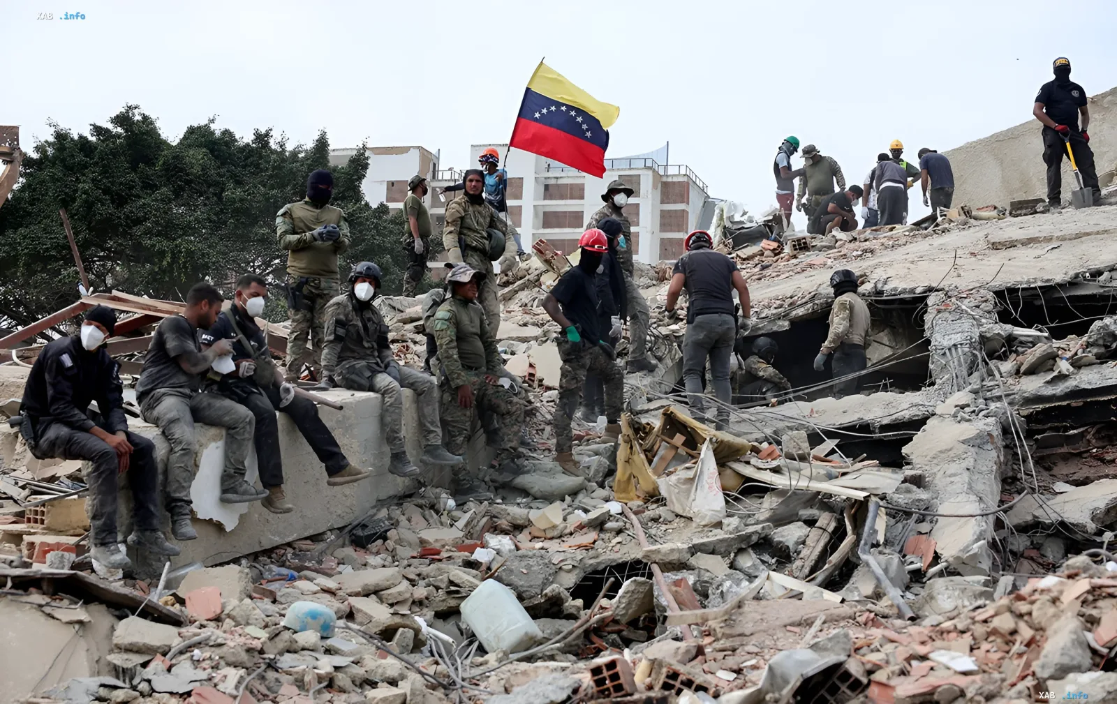Группа спасателей и военных на руинах разрушенного здания в Венесуэле с национальным флагом, участвующих в операции по спасению людей под завалами