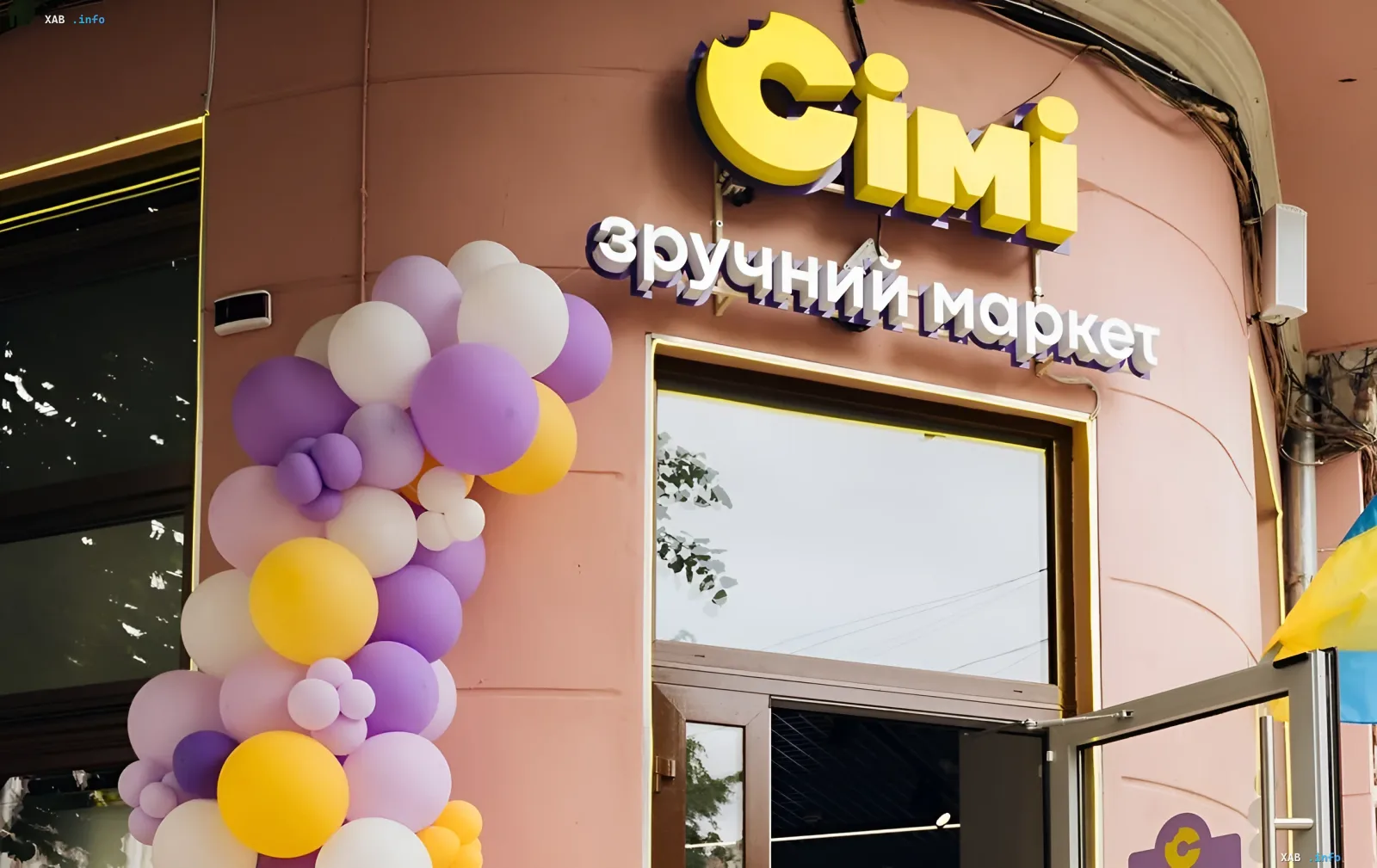 Fassade des Geschäfts der Einzelhandelskette 'Cimi' mit lebendiger gelb-lila Gestaltung und festlicher Ballon-Dekoration, die Wachstum und Anpassung des ukrainischen Handels während des Krieges symbolisiert