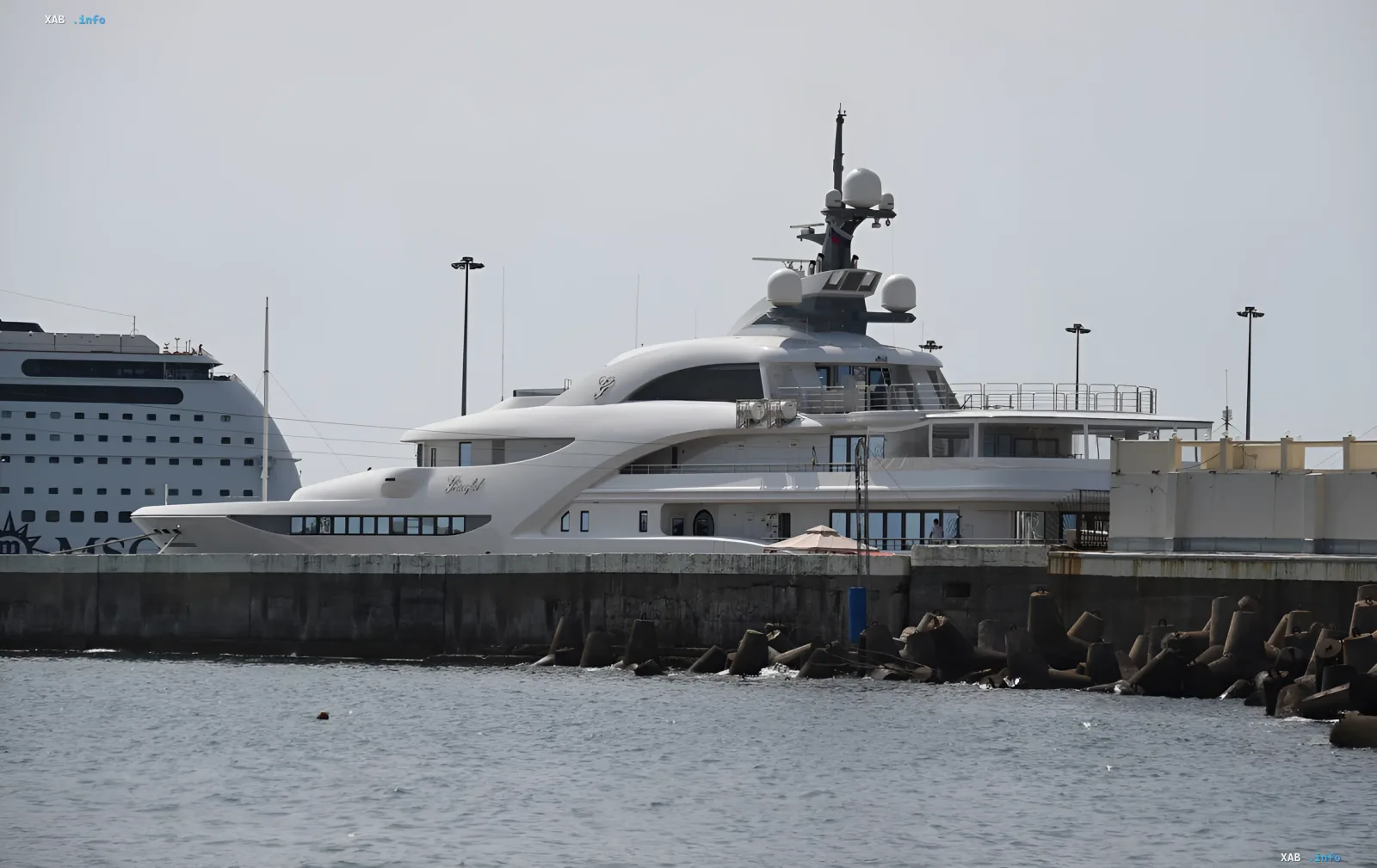 Yacht 'Kosatka' (Project 21900) at anchor in port, side view — white superyacht with distinctive silhouette and superstructure, MSC cruise liner nearby