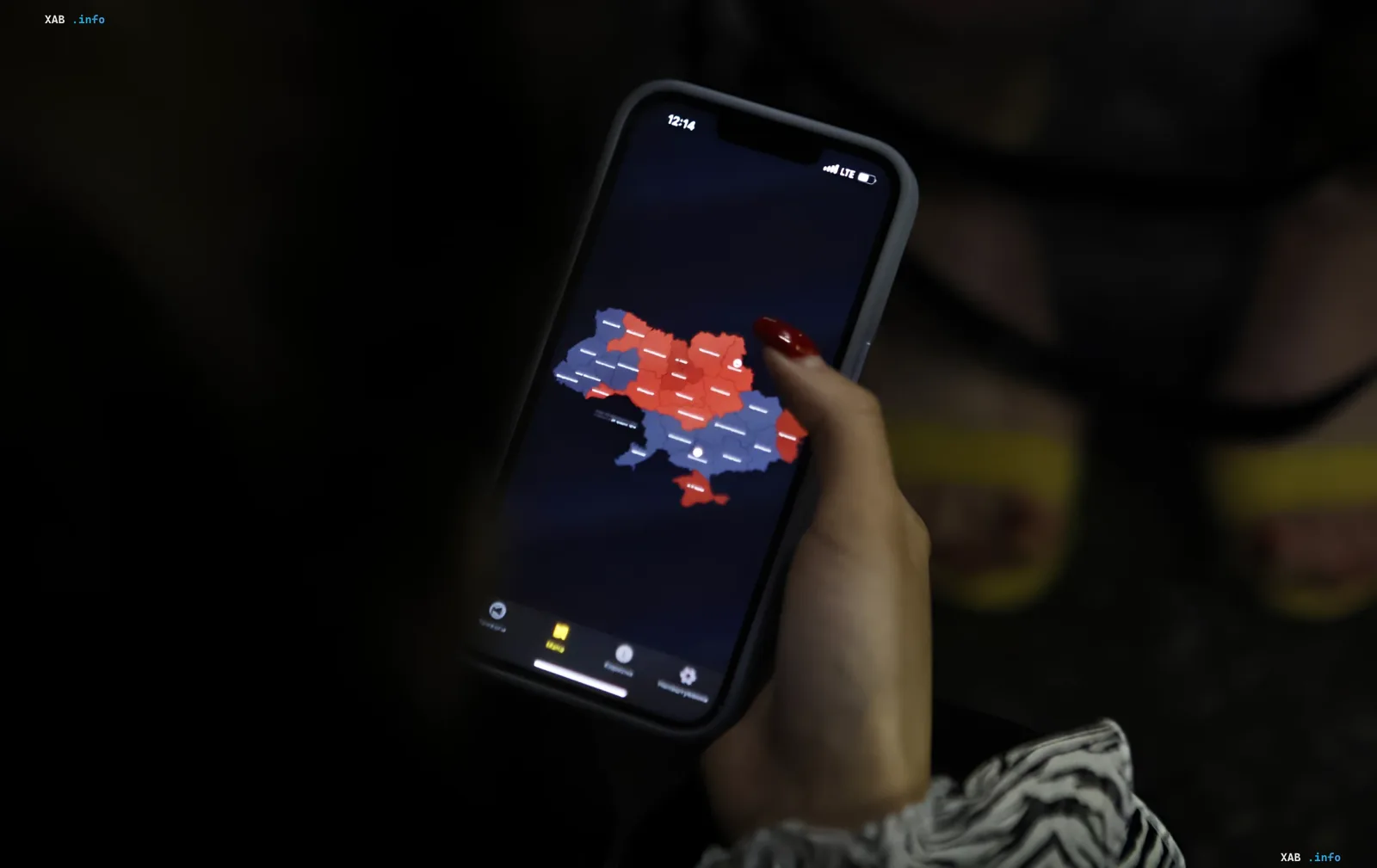 Жінка дивиться на карту України з зонами тривоги на смартфоні в темряві — ілюстрація нового правила виживання в Сумах загрози авіабомб