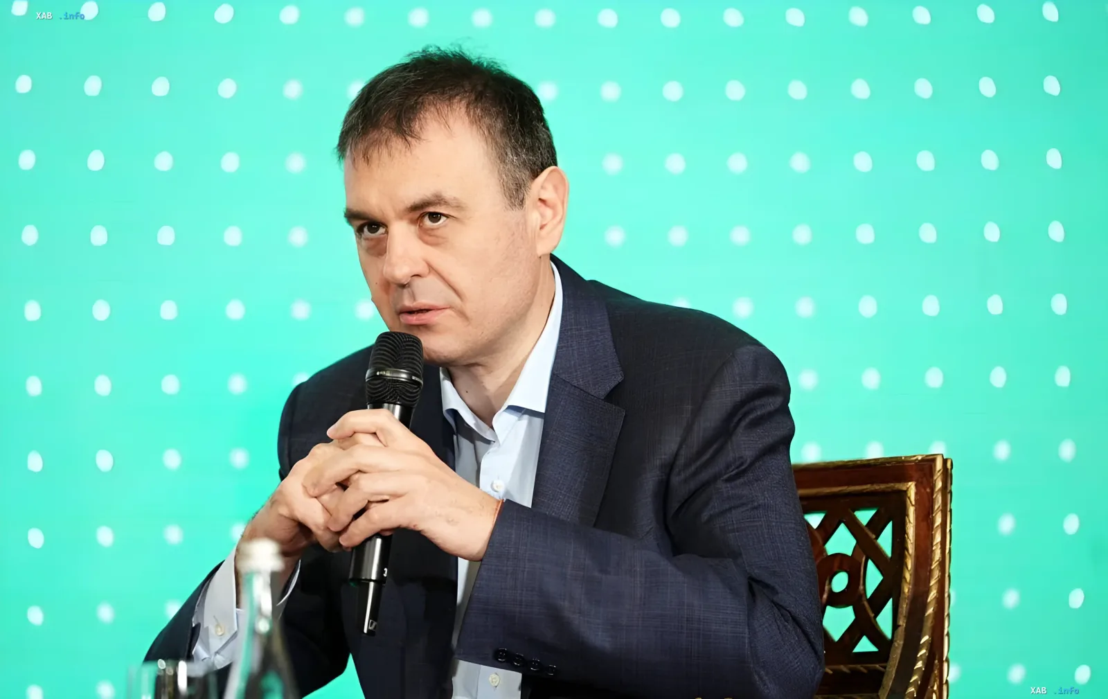 Депутат Верховной Рады с микрофоном на фоне зеленого экрана с точками — обсуждение отмены льгот на посылки и переноса условий МВФ