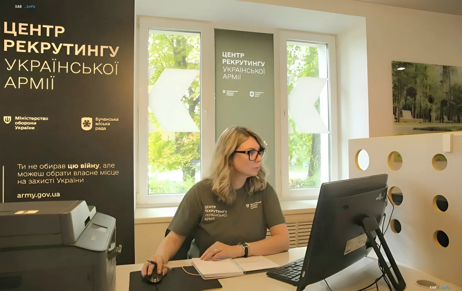 Recruitment Center employee working at a computer in an office with the Ukrainian Ministry of Defense logo and a patriotic slogan on the wall — visual for article on mobilization rules