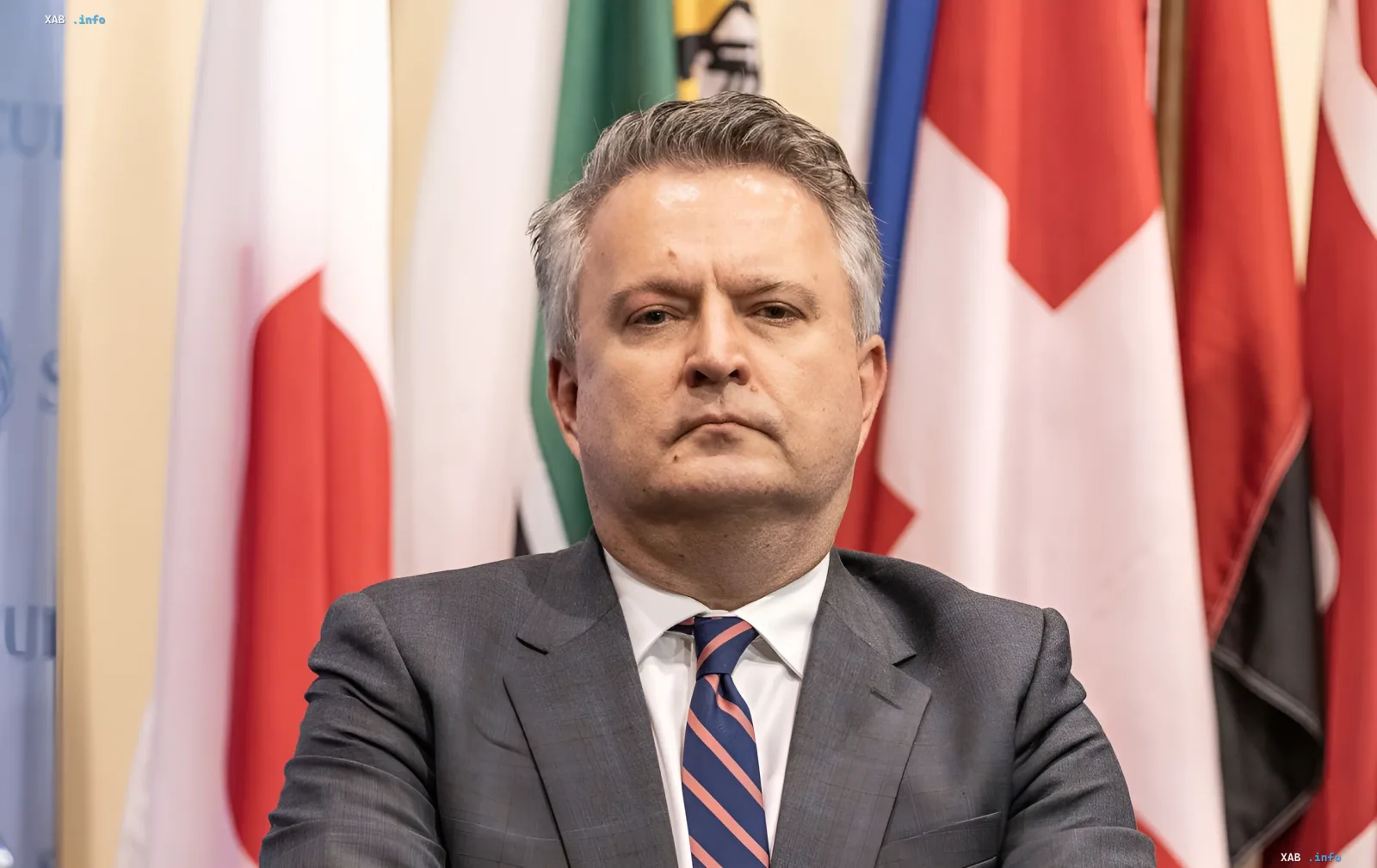 Политик в деловом костюме на фоне флагов, символизирующий пересмотр стратегии США в связи с успехами ВСУ