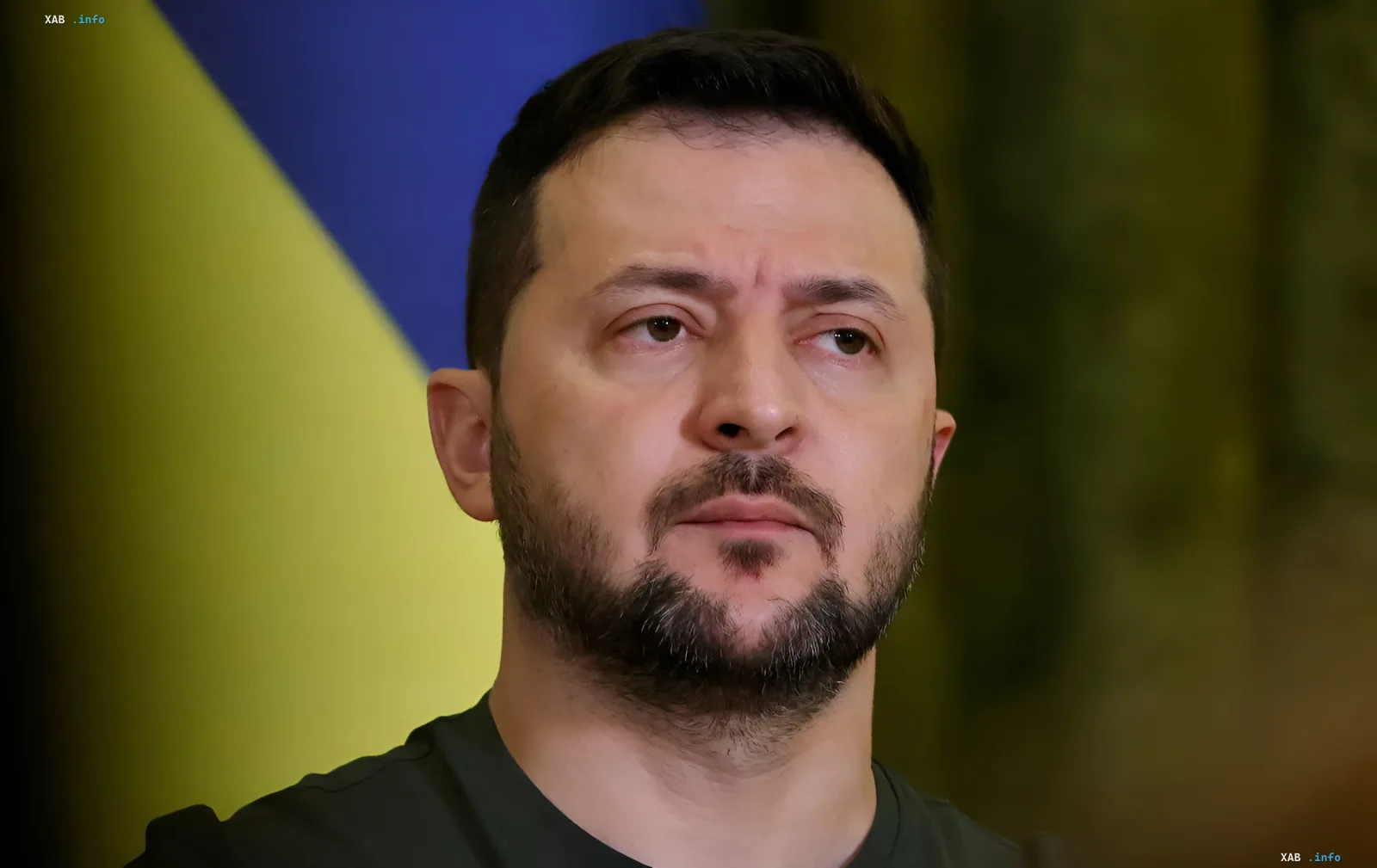 Президент Украины Владимир Зеленский с серьезным выражением лица на фоне украинского флага, обсуждая проблему нехватки ракет Patriot.