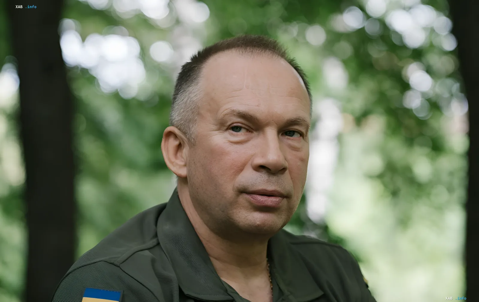 Oberbefehlshaber der Streitkräfte der Ukraine Syrsky in Militäruniform mit ukrainischer Flagge vor einem Hintergrund aus Bäumen, diskutiert die Ergebnisse des ersten Halbjahres 2026