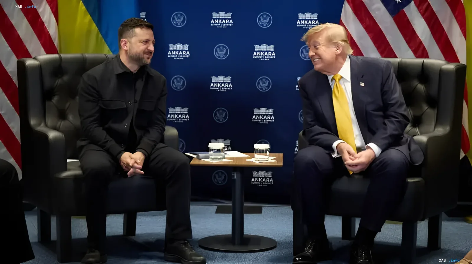 Volodymyr Zelenskyy and Donald Trump sitting in chairs with US and Ukrainian flags in the background, smiling at each other during a NATO summit meeting