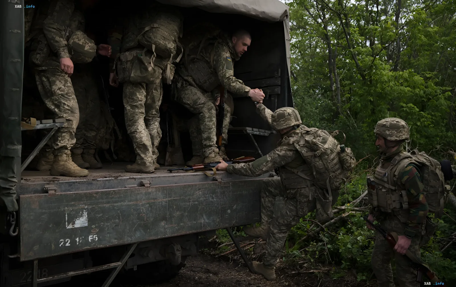 Украинские военные выходят из грузовика, один помогает другому, символизируя поддержку и заботу государства о ветеранах и освобожденных из плена.