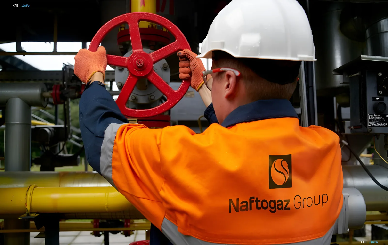 Работник Нафтогаз Групп в оранжевой спецодежде с логотипом компании управляет красным вентилем на газопроводе, символизируя доступ к услугам и новые способы оплаты через Национальный кэшбек