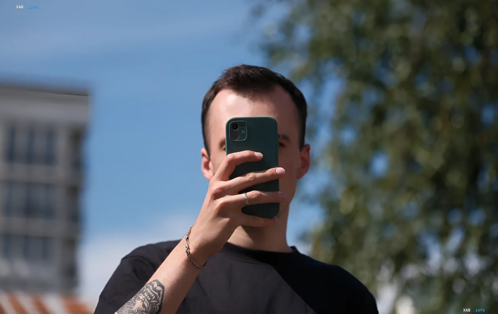 Молодой человек фотографирует себя на смартфон на фоне городского пейзажа, иллюстрируя тему контроля над иностранными SIM-картами в России.