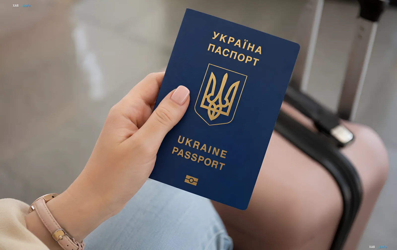 Украинский паспорт в руке человека с чемоданом на фоне — символ миграции и временной защиты украинцев в ЕС