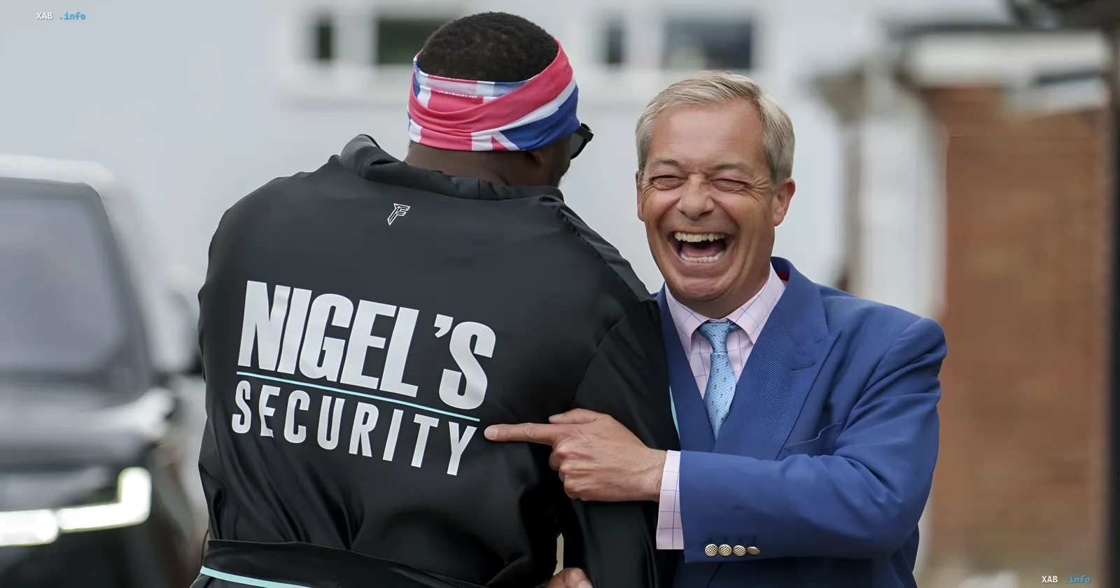 Ниджель Фарадж смеётся, указывая на надпись «NIGEL’S SECURITY» на куртке охранника с британским банданой — символ его попытки контролировать нарратив перед скандалом