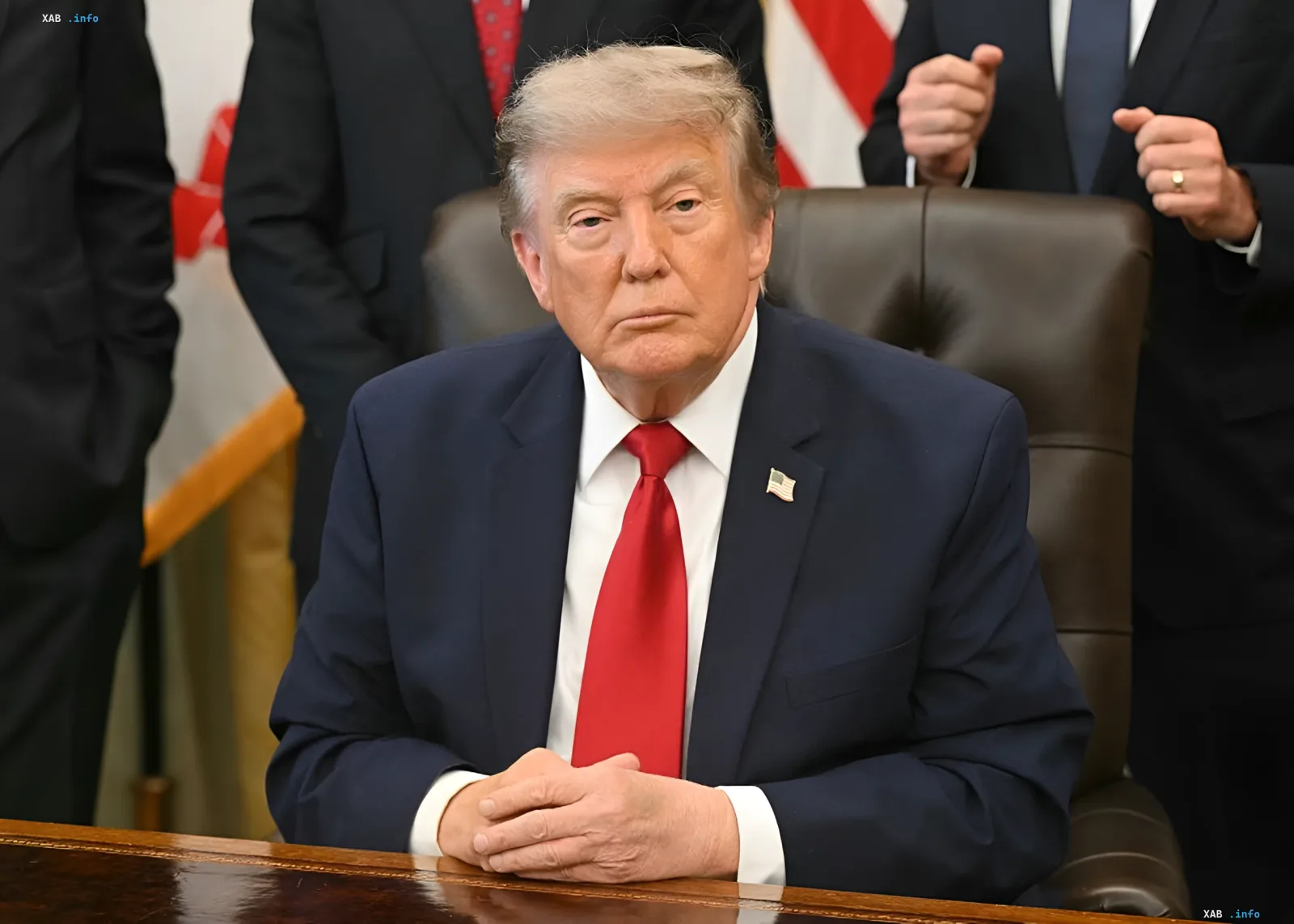 Donald Trump in einem blauen Anzug und roter Krawatte sitzt an einem Tisch, im Hintergrund US-Flaggen und andere Beamte – Moment der offiziellen Benachrichtigung des Kongresses über die Wiederaufnahme des Krieges mit dem Iran
