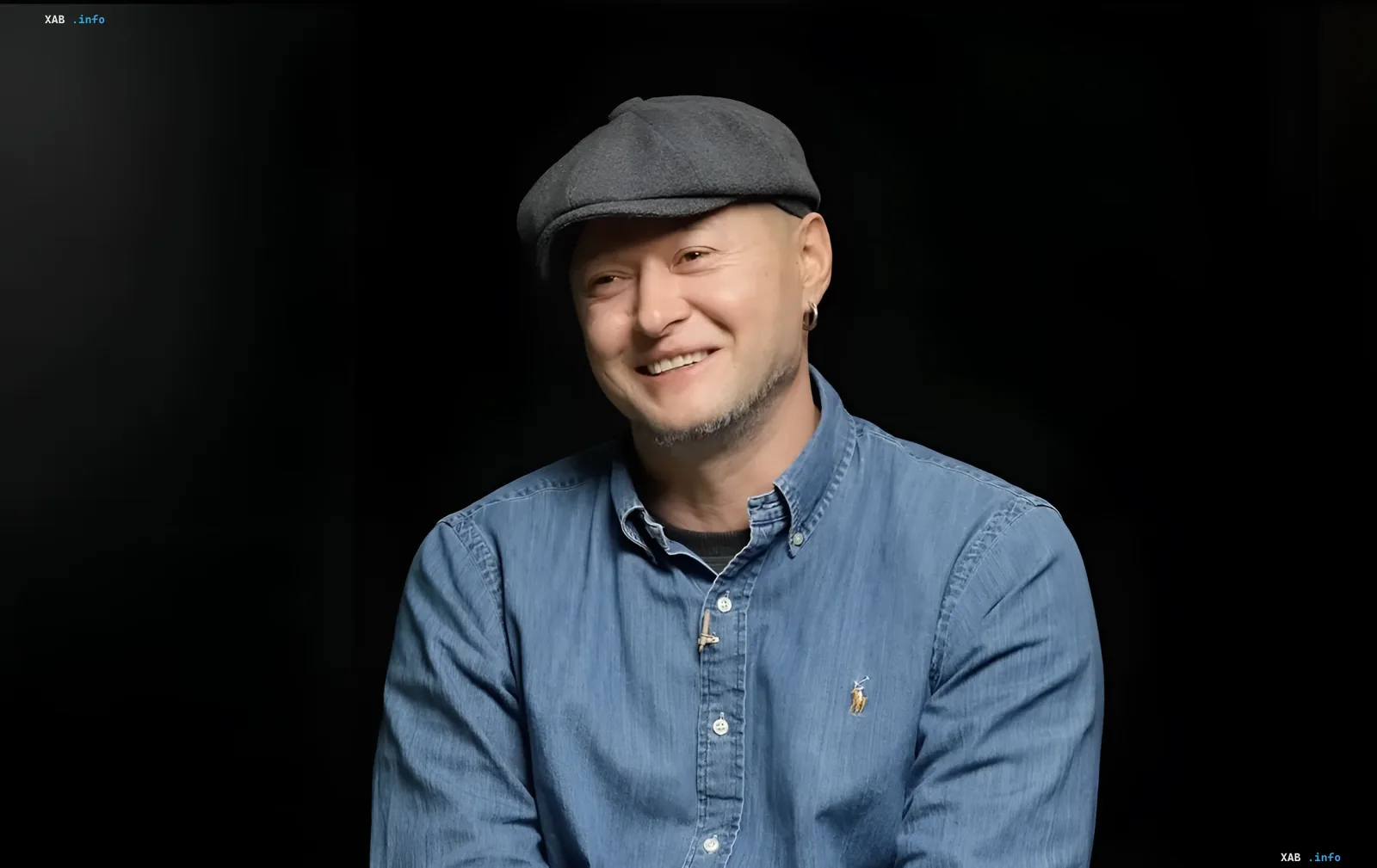 Andriy Khlyvnyuk, leader of the band Bumbocks, in a blue shirt and gray cap, smiling against a black background, awarded the title of Honored Artist of Ukraine