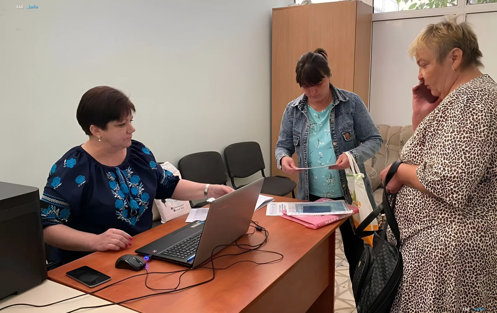 Frau erhält neues Sozialhilfeausweis von Angestellten am Laptop — Bearbeitung ab Mai 2026