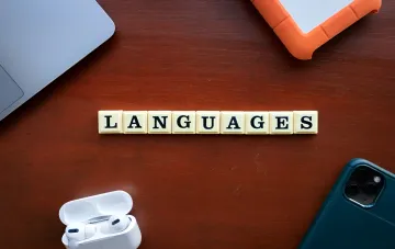 Слово LANGUAGES из кубиков на деревянном столе рядом с ноутбуком, телефоном и наушниками — символ создания языков ИИ