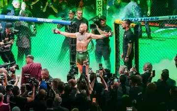 Конор Макгрегор у октагоні UFC з піднятими руками на тлі зеленого диму, вимагає скасувати бій з Холлоуєм та повернення ставок