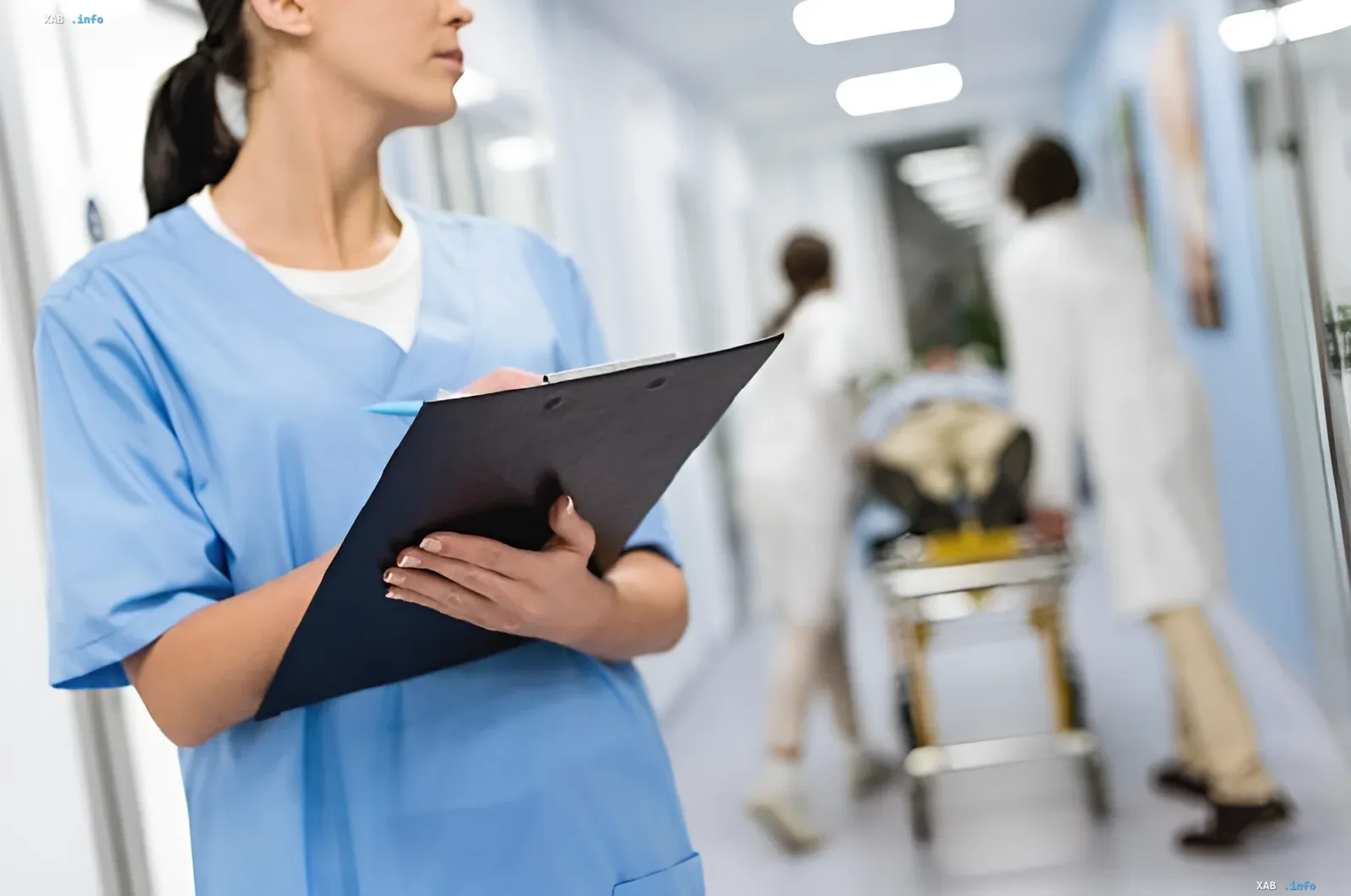 Krankenschwester in blauer Uniform hält Tablet im Krankenhausflur, im Hintergrund verschwommene Ärzte und Trage; Illustration zum NY-Prozess: Kann KI Pflegepersonal ersetzen?