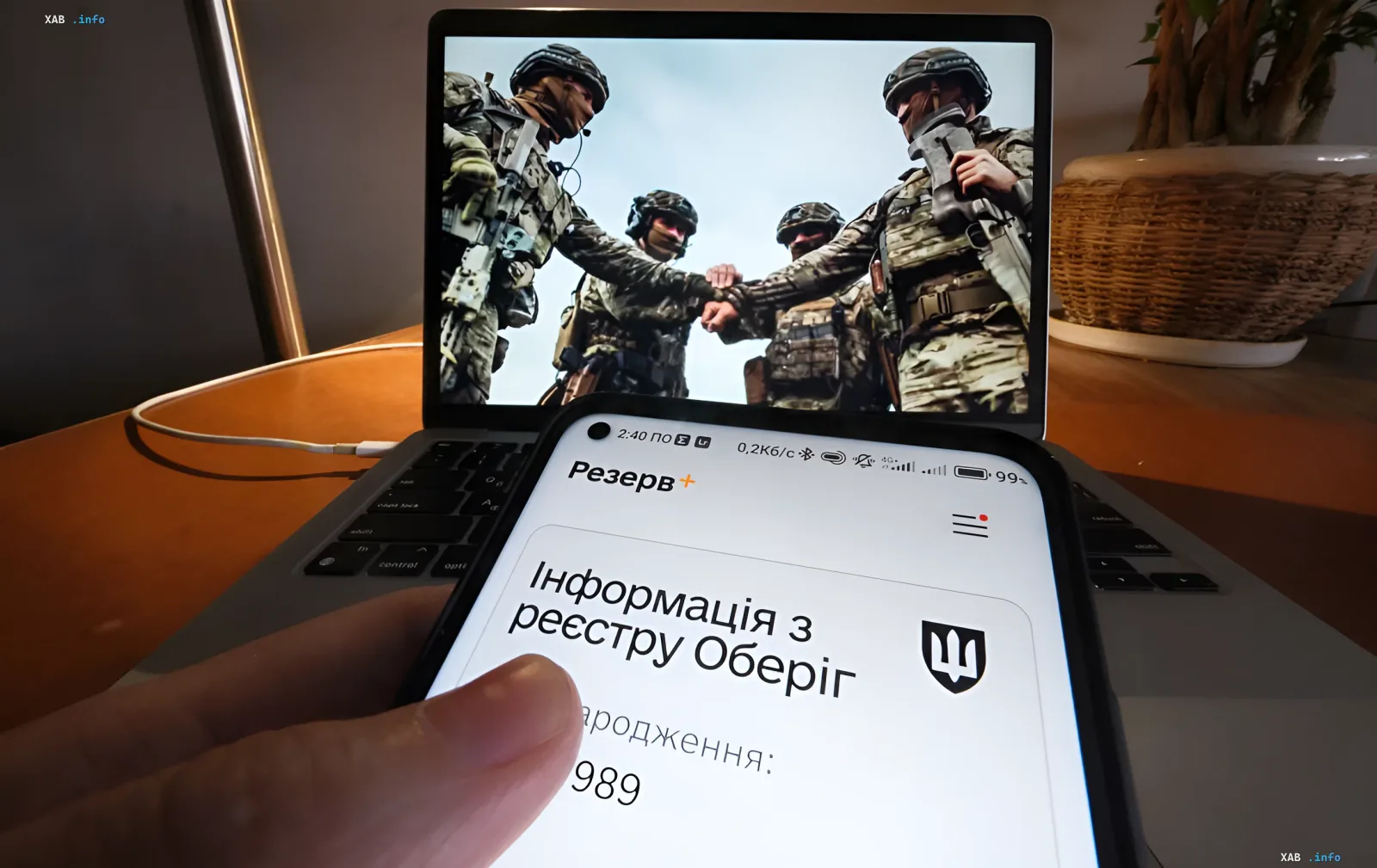 Smartphone mit geöffnetem 'Rezerv+'-App und Daten aus dem Oberyg-Register, im Hintergrund Laptop mit Bild ukrainischer Soldaten — Symbol für neue Verträge und garantierte Mobilisierungsaufschub