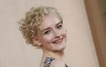 Actress Julia Garner with short blonde hair and gold earrings, smiling on the red carpet