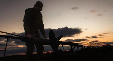 Ukrainian soldier prepares an attack drone for launch against a sunset backdrop, symbolizing a new era in the war against Russian logistics