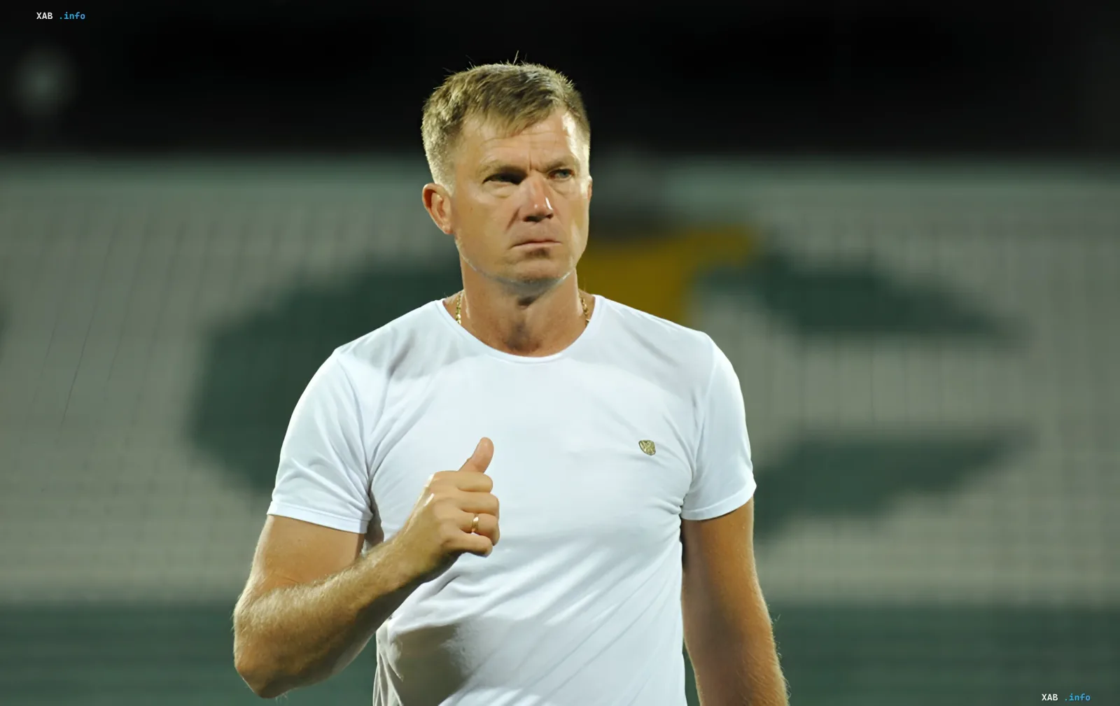 Yuriy Maksimov in a white t-shirt on a stadium background, confidently gesturing while discussing the upcoming match 'Dynamo' — 'Universitatea'