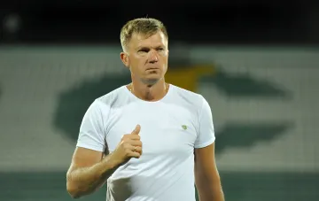 Yuriy Maksimov in a white t-shirt on a stadium background, confidently gesturing while discussing the upcoming match 'Dynamo' — 'Universitatea'