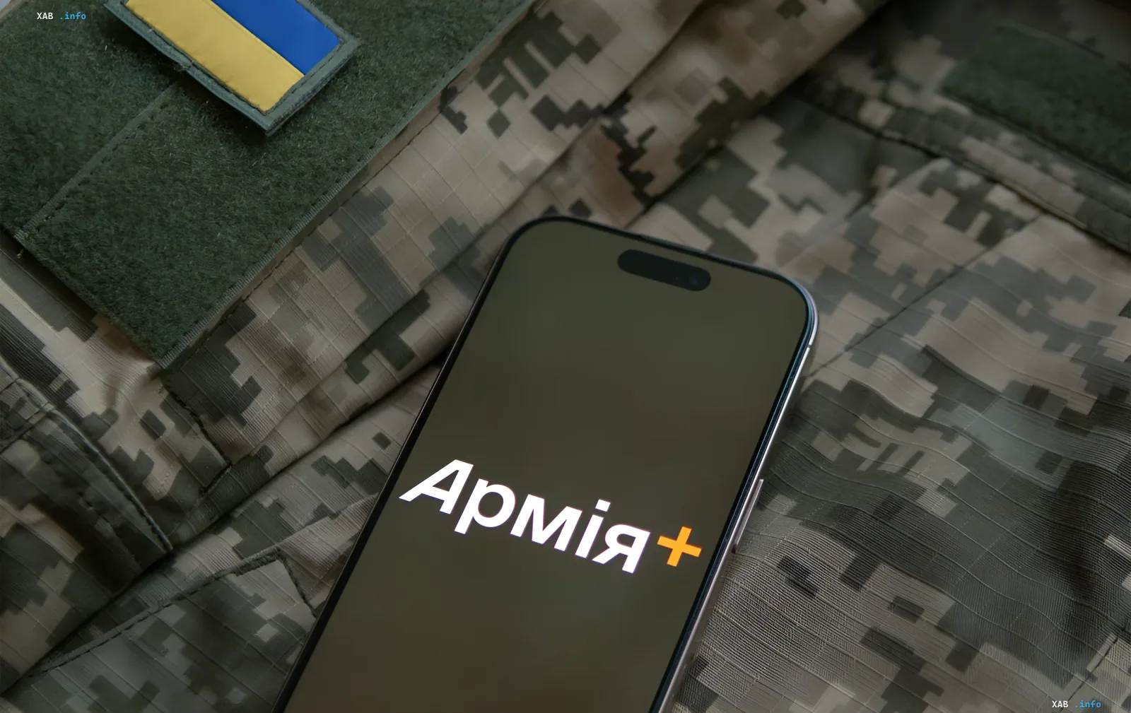 Смартфон із логотипом додатку «Армія+» на фоні військової форми з українським прапором — символ цифрового військового квитка