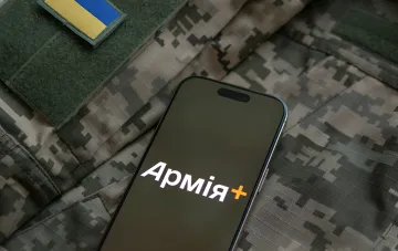 Смартфон із логотипом додатку «Армія+» на фоні військової форми з українським прапором — символ цифрового військового квитка