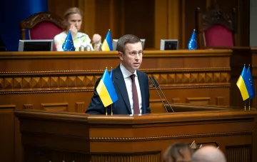 Сергій Корецький виступає в парламенті на тлі прапорів України та ЄС, анонсувавши дату засідання МВФ щодо виділення траншу в 690 млн доларів