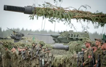 Військові НАТО в камуфляжі зі зброєю на тлі танків та військової техніки під час навчань у Балтії