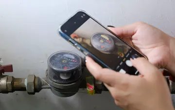 Жінка фотографує лічильник води смартфоном, демонструючи актуальну проблему з повіркою приладів обліку в Україні