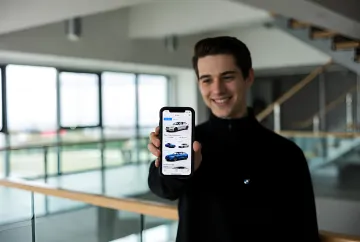 Молодой человек показывает на смартфоне приложение BMW с выбором моделей автомобилей, демонстрируя использование ИИ для подбора идеального авто